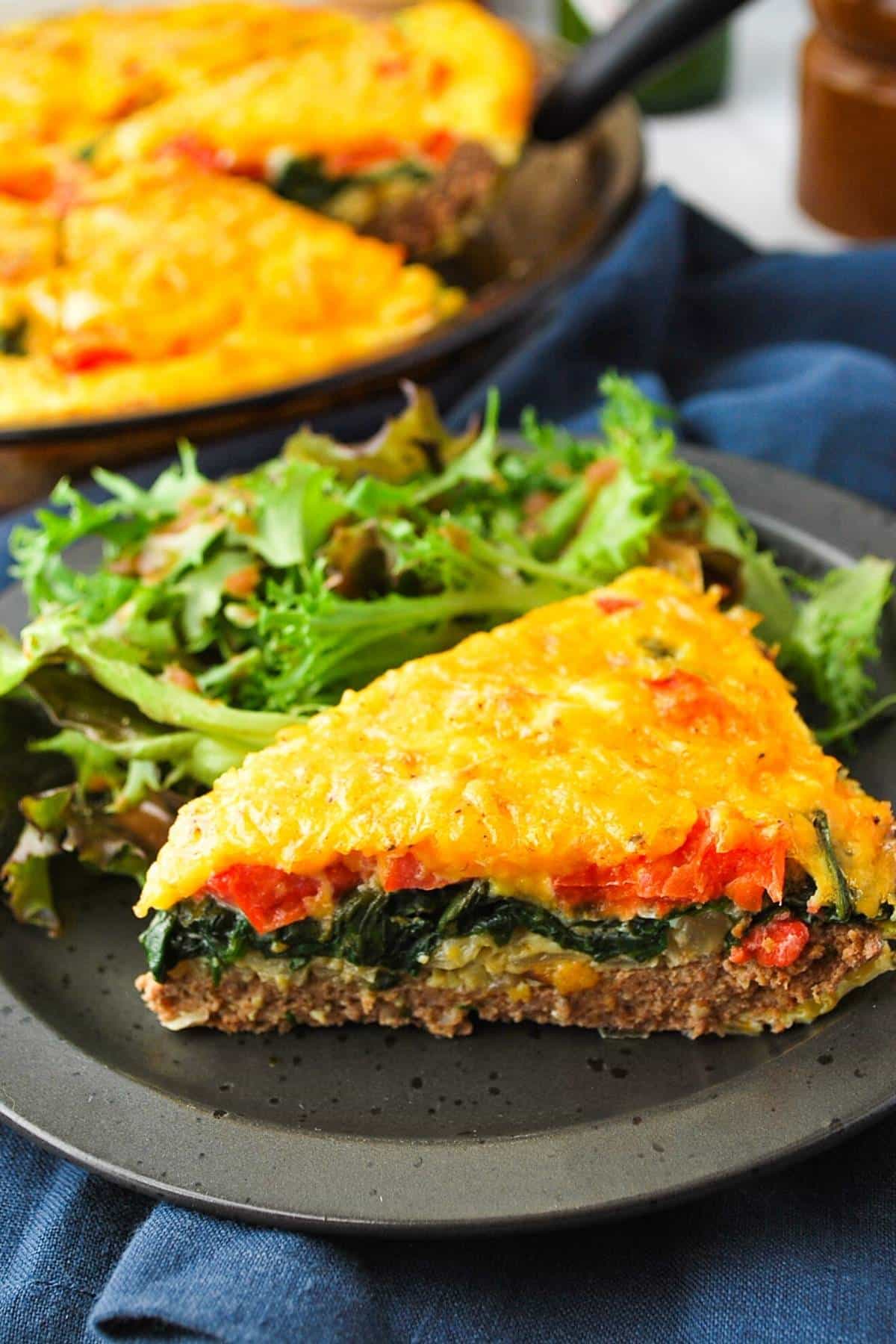 a slice of high protein quiche with salad greens on a plate