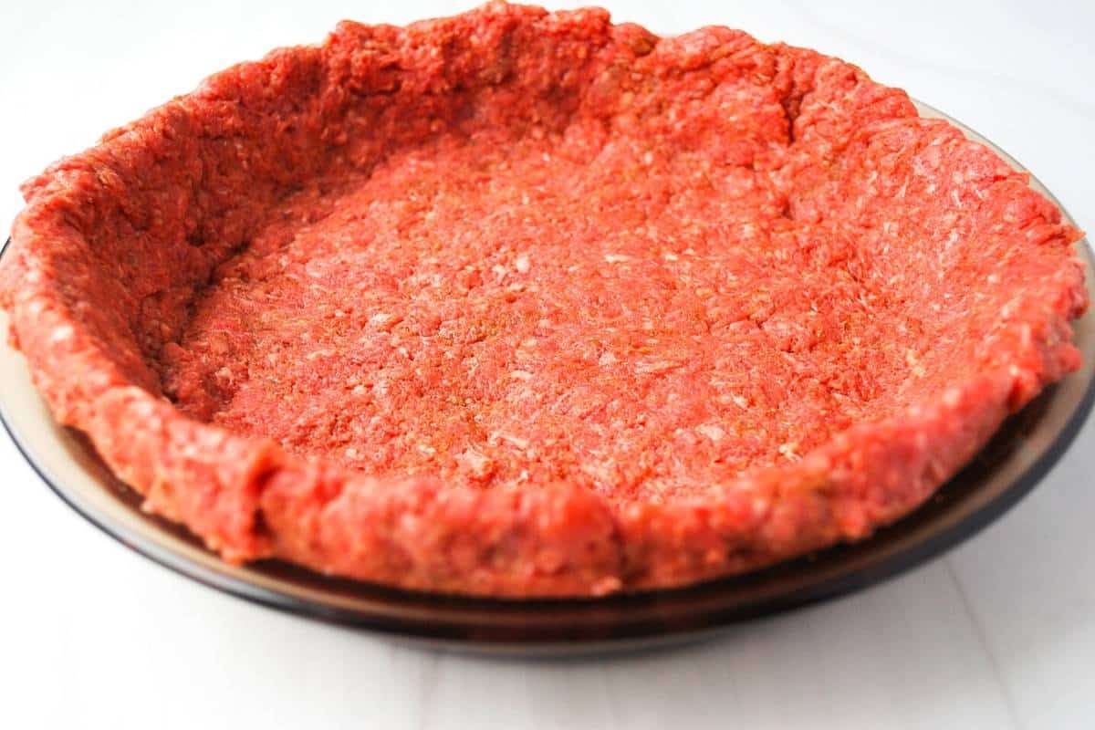 ground sirloin beef quiche crust pressed into a pie plate ready to cook