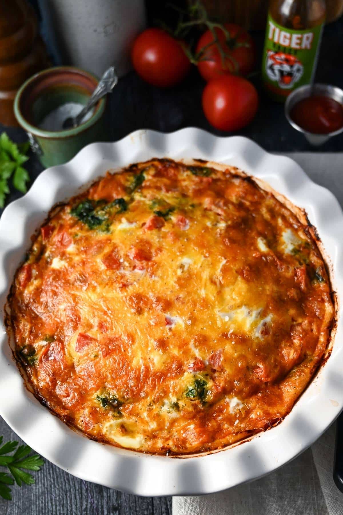 a cooked cheeseburger quiche with tomatoes, salt and pepper in the background