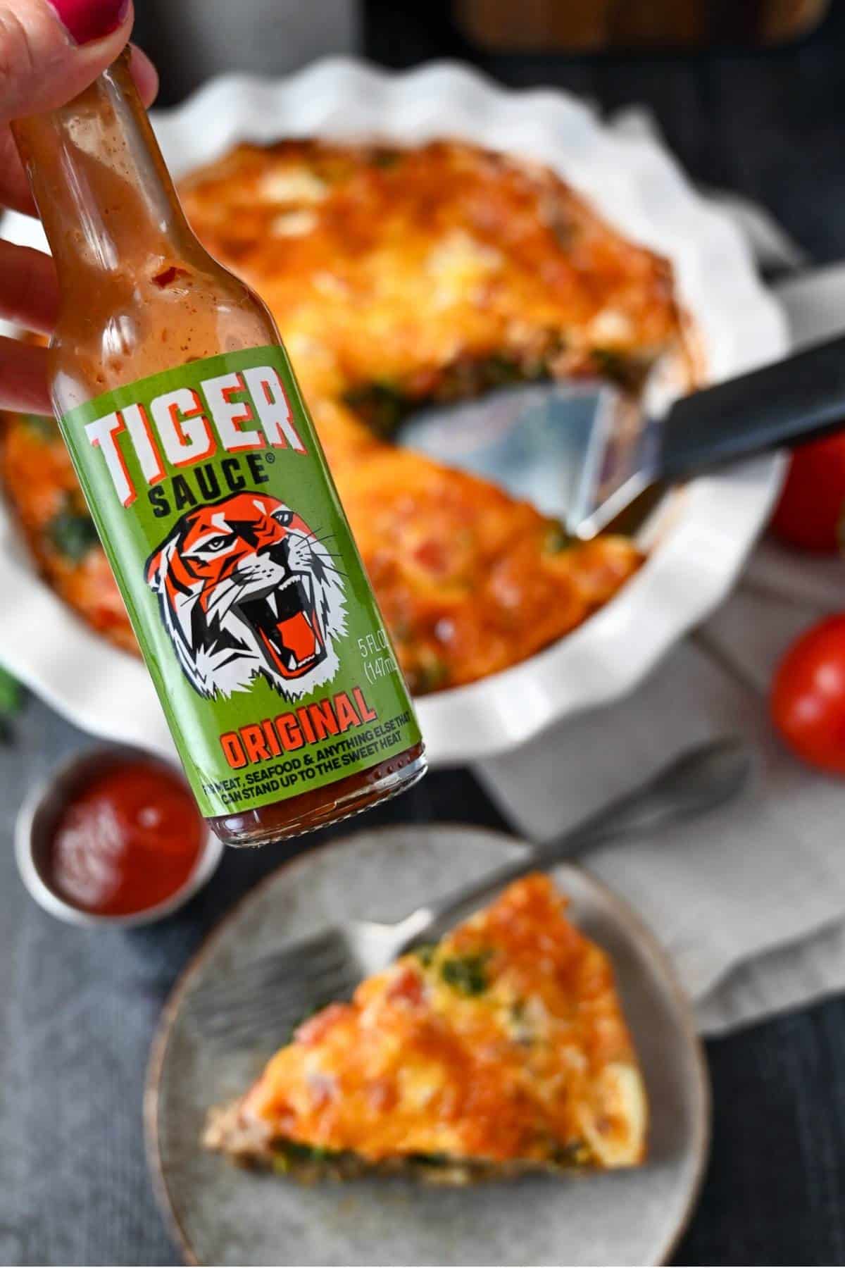 holding up a bottle of Tiger Sauce over a quiche and a served slice of quiche