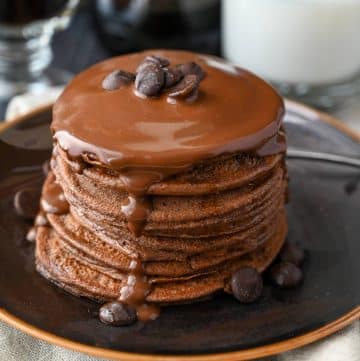 close up of a stack of protein chocolate pancakes with melted chocolate poured on top with a garnish of chocolate chips