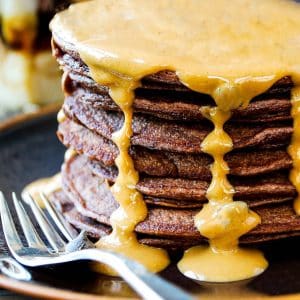 close up side view of a stack of chocolate protein pancakes with peanut butter drizzled on top