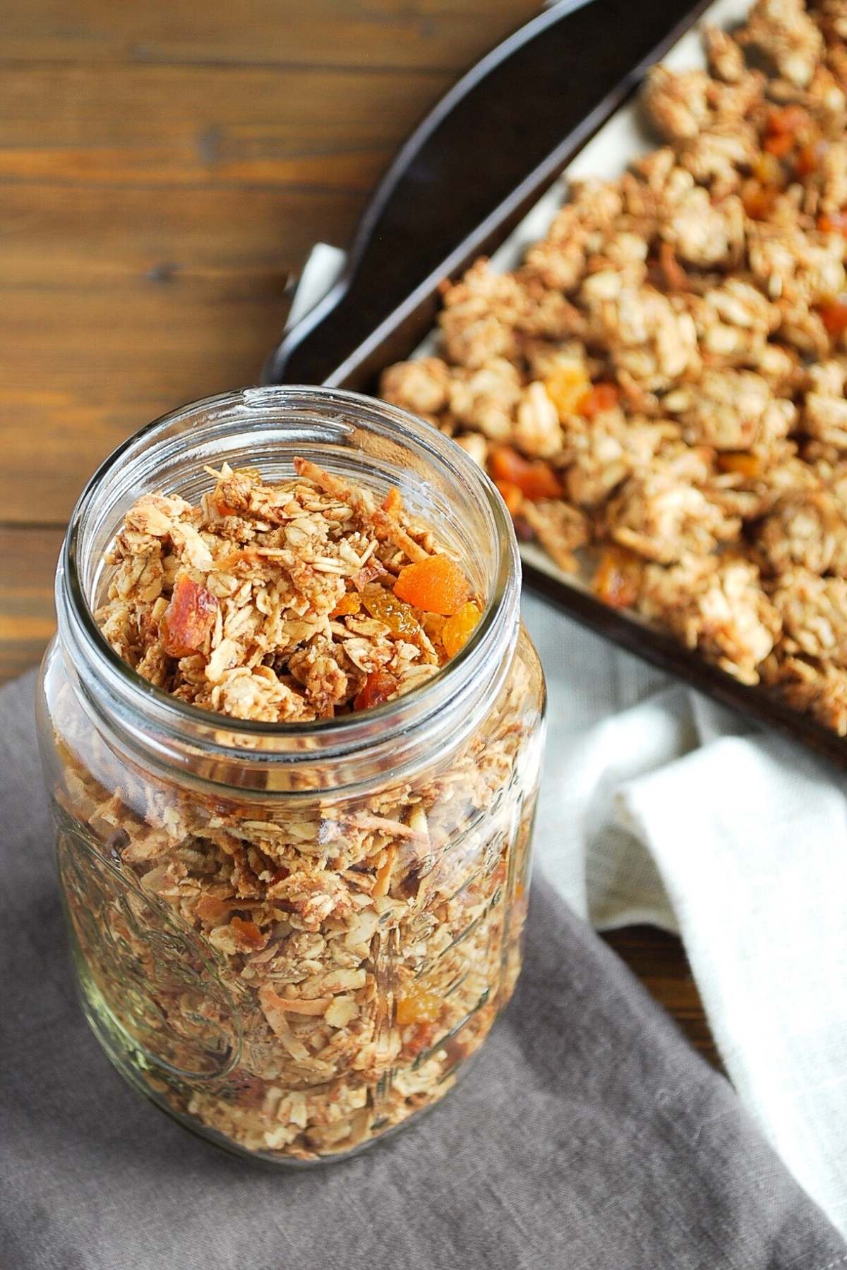 close up of a large mason jar full of homemade granola with a pan of granola behind it