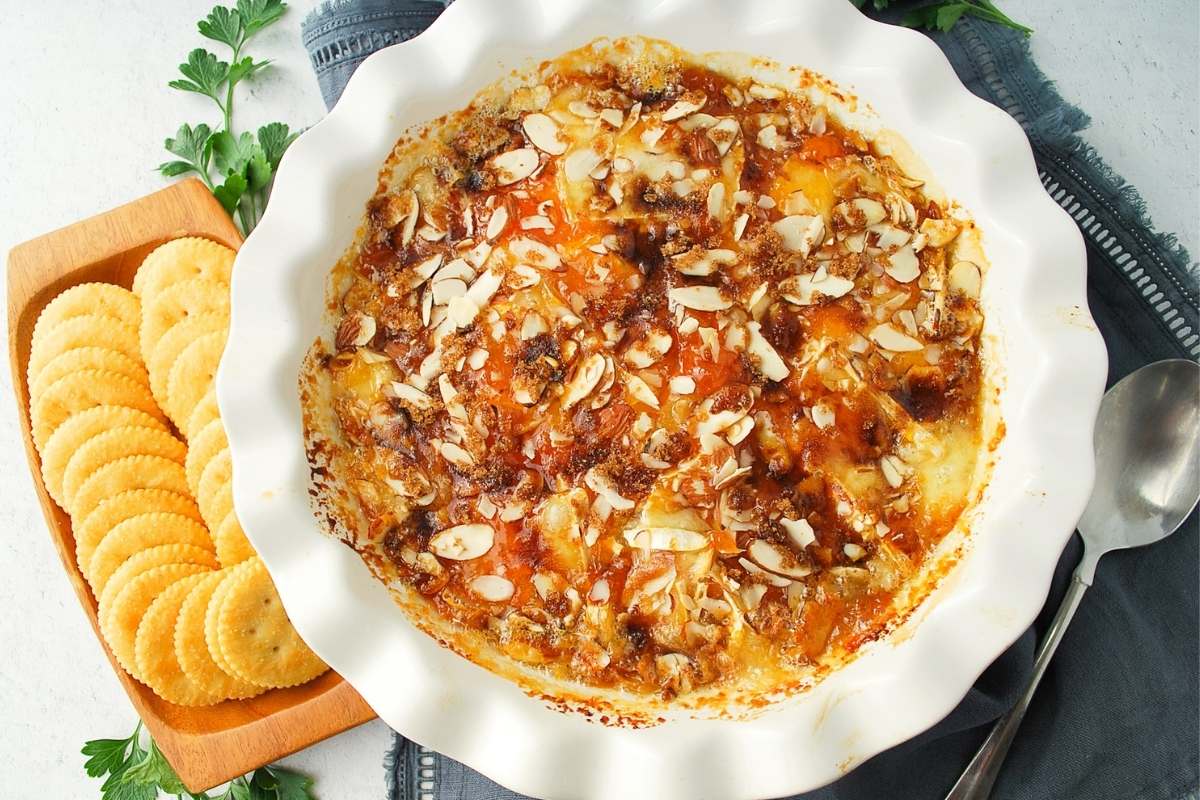 baked brie topped with brown sugar, jam and almonds in a pie plate served with crackers