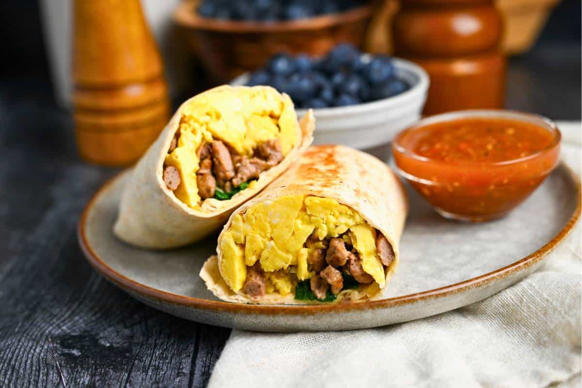a stacked egg and sausage burrito on a plate with berries and salsa on the side