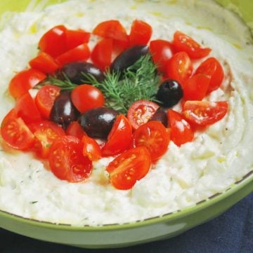 Whipped feta dip topped with chopped cherry tomatoes, olives, and fresh dill in a bowl