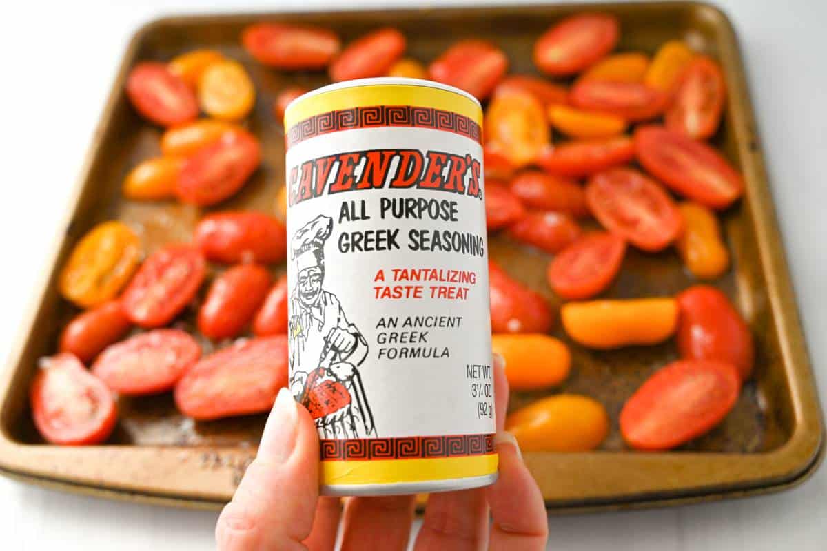 tomatoes on a baking sheet with a jar of Greek seasoning
