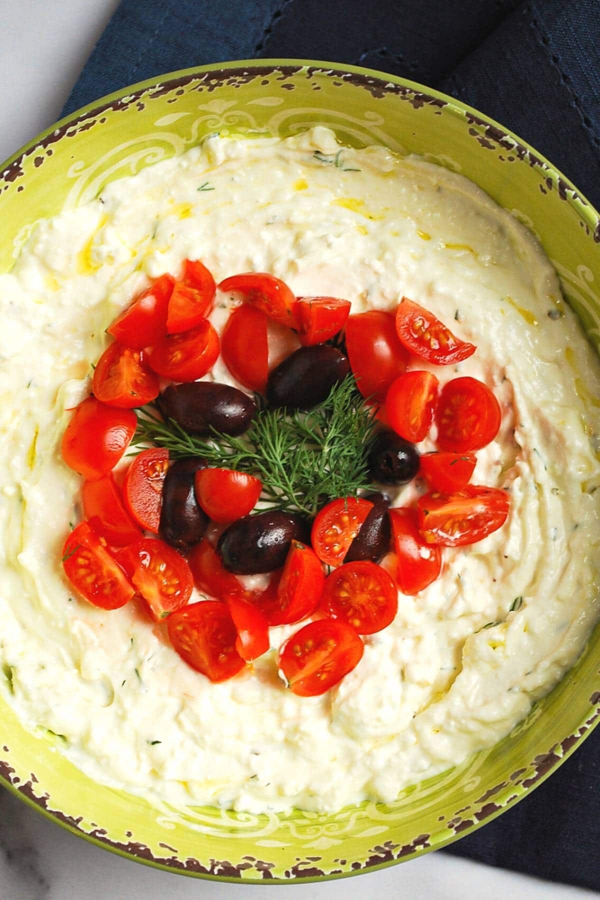 overhead photo of a bowl of whipped feta dip with Greek yogurt, tomatoes, olives, and tomatoes
