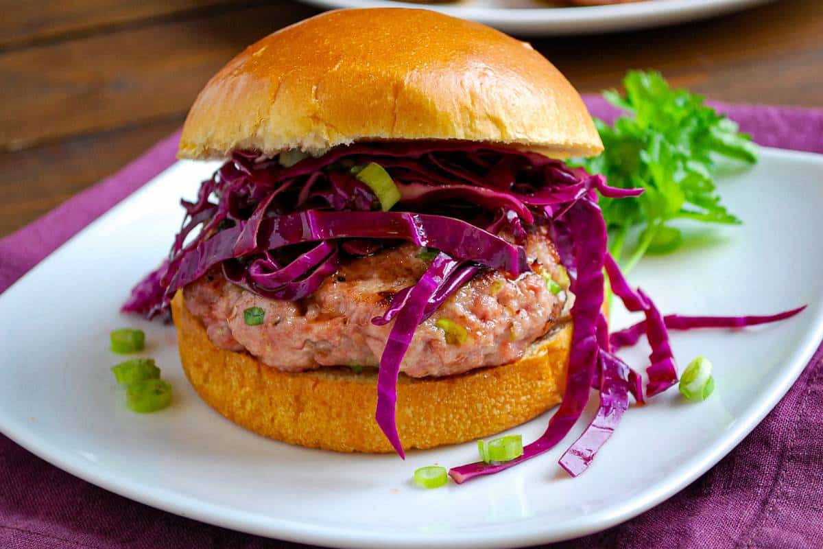 an asian pork burger on a brioche bun with asian red cabbage slaw on a white plate
