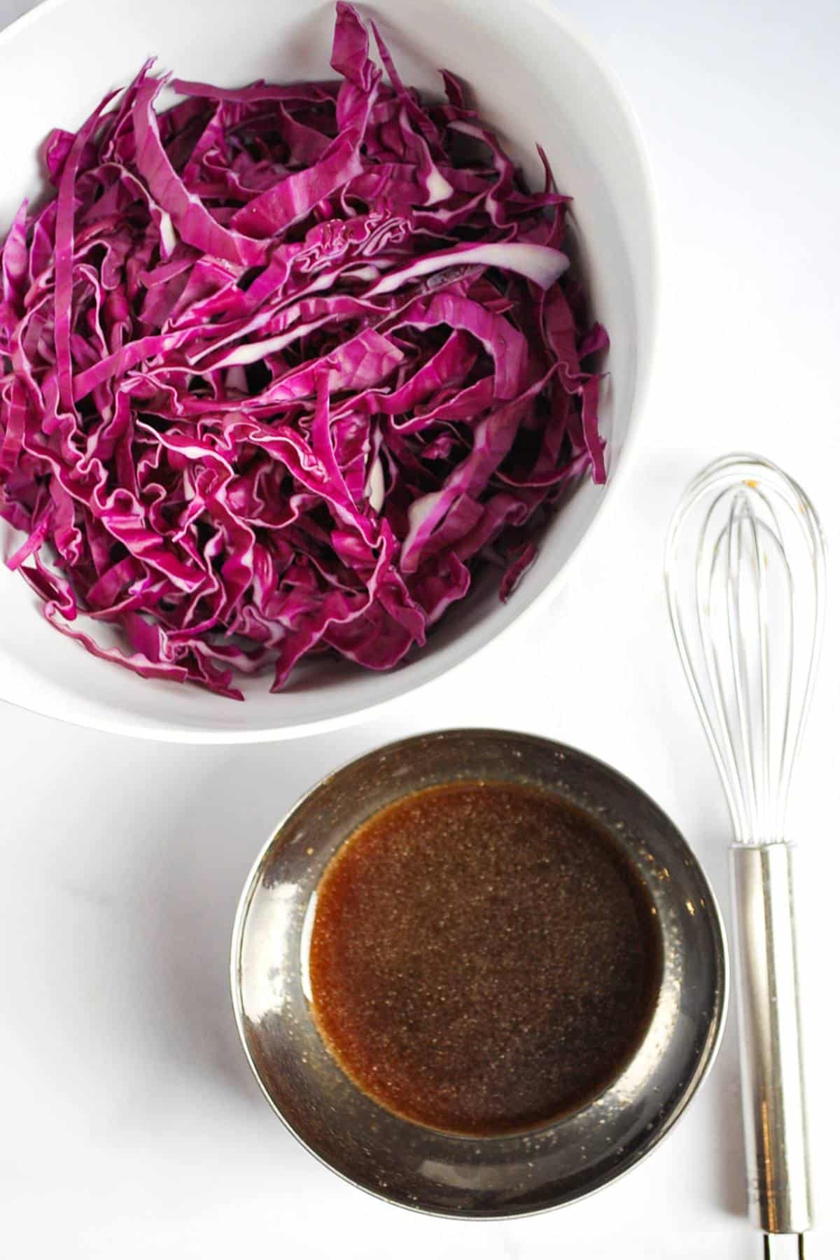 red cabbage shredded in a bowl with a bowl of Asian slaw dressing