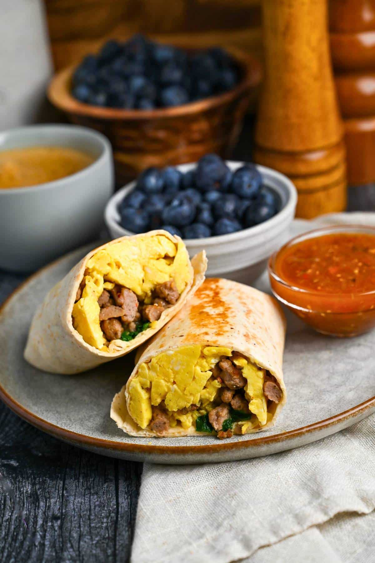 a high protein breakfast burrito sliced in half on a plate with berries and salsa