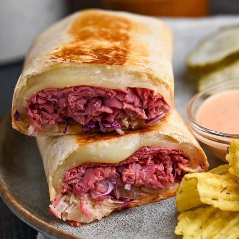 a sliced corned beef reuben wrap with chips and a dish of dressing