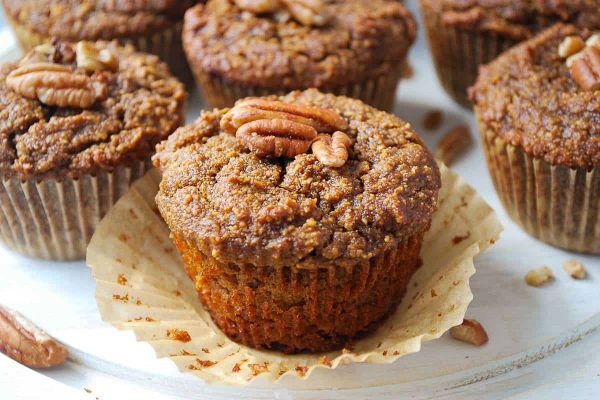 an almond flour pumpkin muffin topped with pecans with the wrapper peeled back