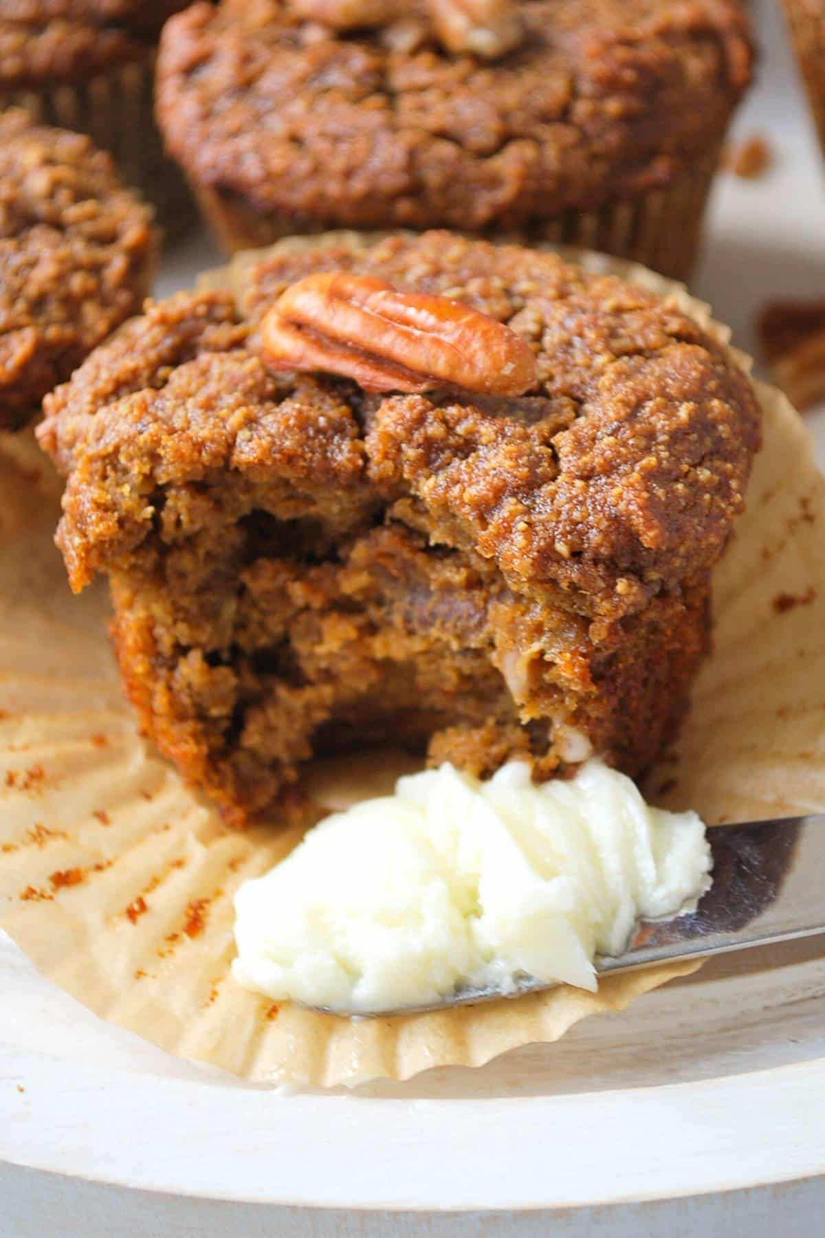 a photo with a pumpkin muffin with a bite out of it with a knife full of butter beside it