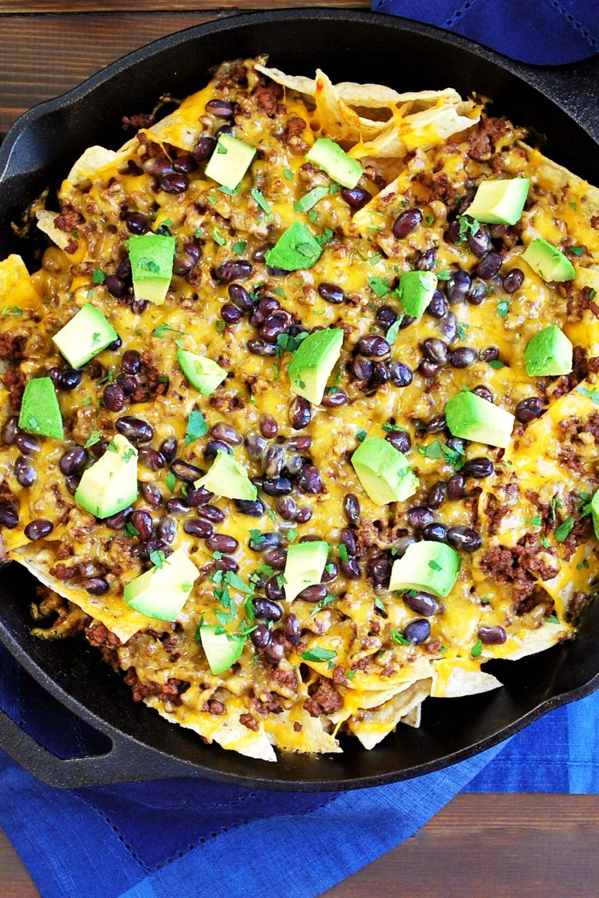 overhead photo of a skillet full of cooked beef nachos with avocado on top