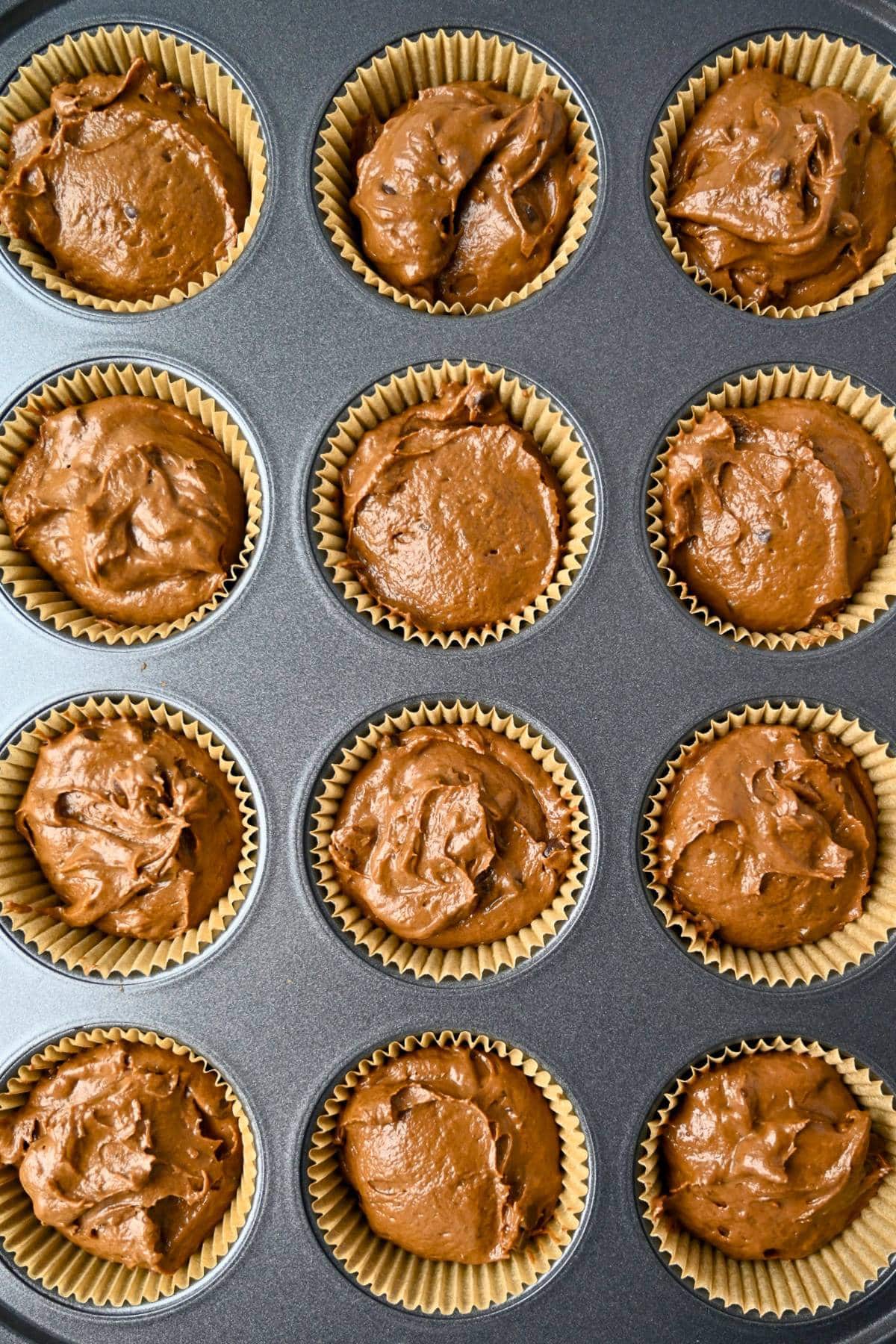 chocolate muffin batter scooped into paper liners in a muffin pan