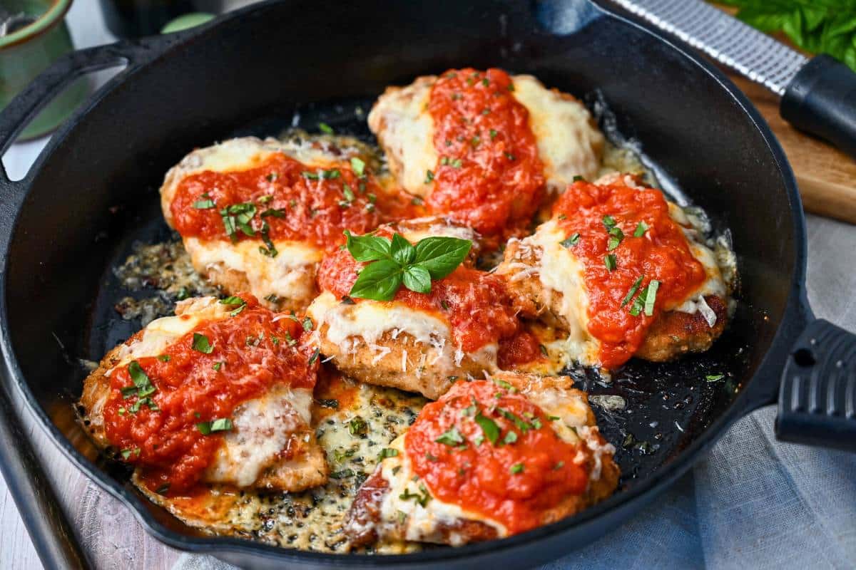 side view of a finished pan of cooked chicken parm in a heavy cast iron pan