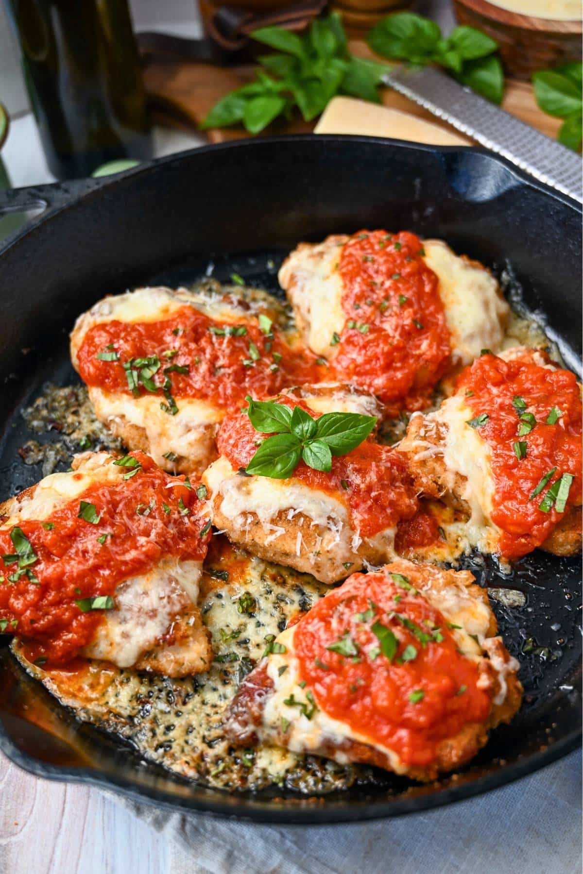a cast iron skillet with cooked chicken parmesan and a sprig of basil on top
