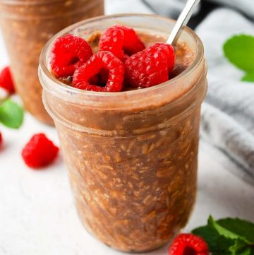 close up of a mason jar with chocolate protein overnight oats with a spoon and fresh raspberries