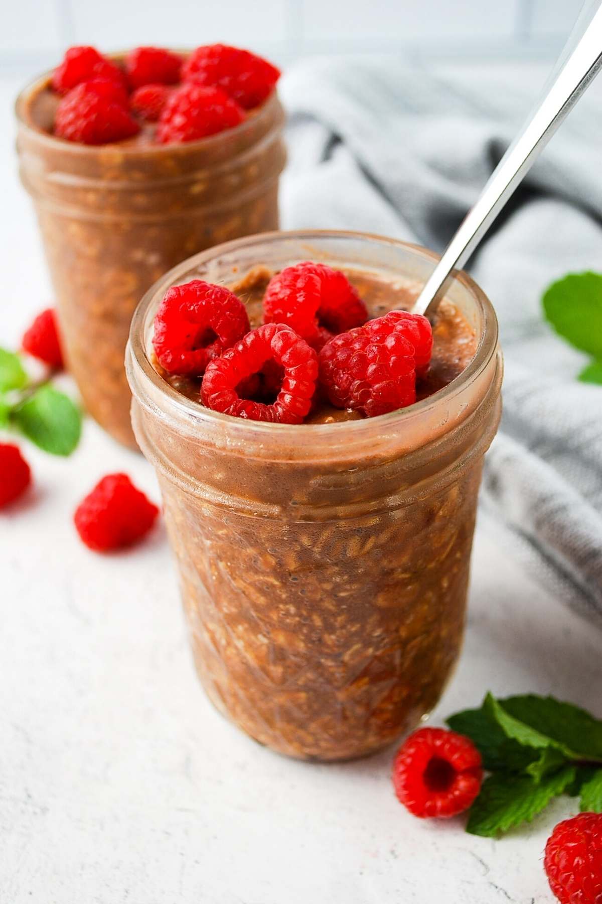 two jars of chocolate protein overnight oats topped with raspberries 