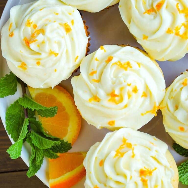 orange cupcakes with orange zest on the top on a platter with mint and orange slices