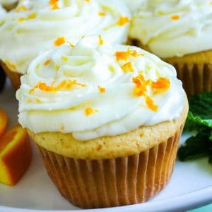 close up of an orange cupcake on a platter topped with orange zest