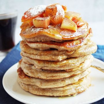 stack of pancakes dripping with syrup topped with chopped baked apples on a plate