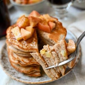 a stack of apple protein pancakes with a bite cut out on a fork
