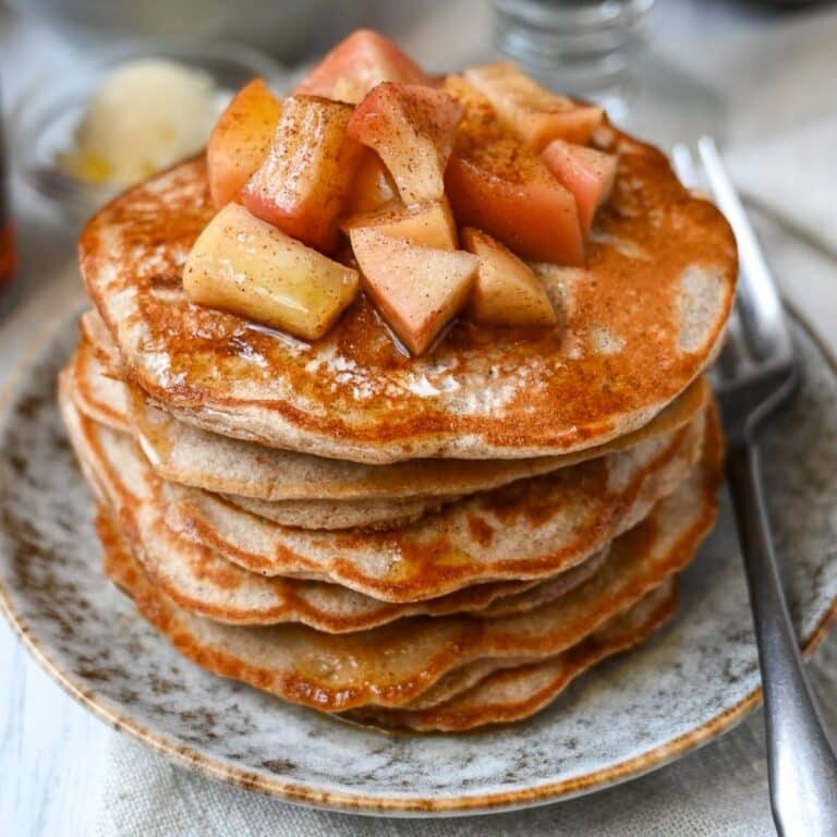 close up of a tall stack of pancakes with apples on top