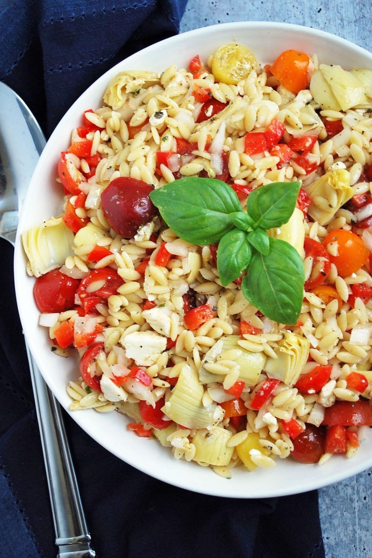 lemon orzo pasta salad topped with a sprig of basil in a large white bowl