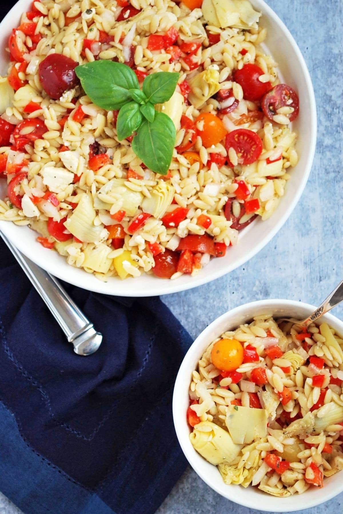 A large serving bowl of lemon orzo pasta salad with a small bowl of pasta salad next to it