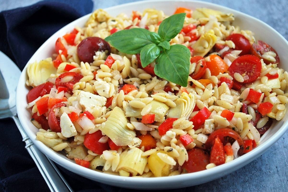 side view of a serving bowl filled with summer orzo pasta salad and a serving spoon