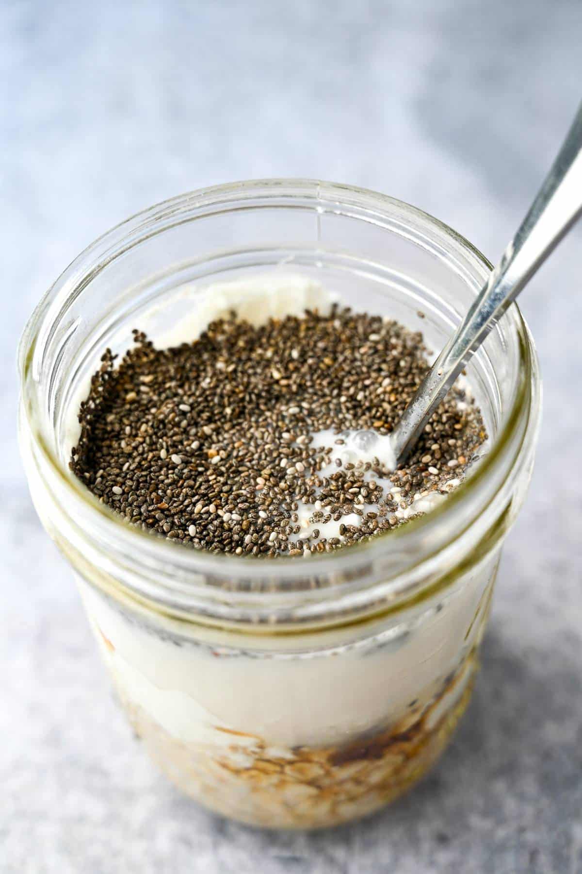 overnight oats ingredients with egg whites, chia seeds, and yogurt in a jar with a spoon