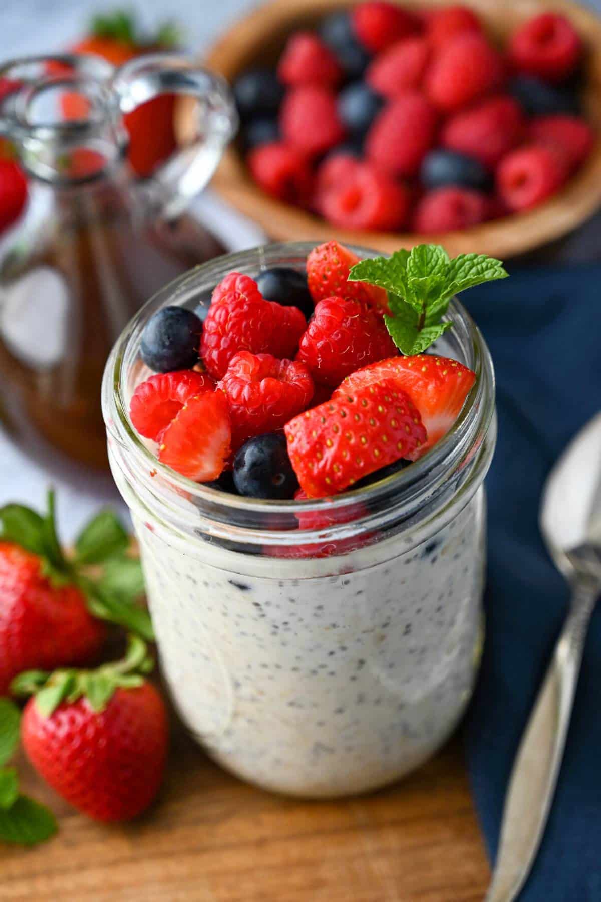 protein oats in a mason jar with blueberries, strawberries, and raspberries on top with a bowl of berries behind it