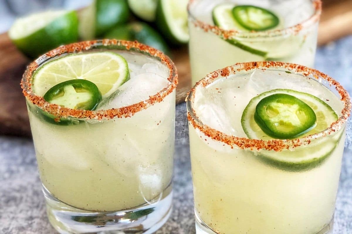 close up of spicy margaritas with a salted Tajin rim, fresh jalapenos, and lime