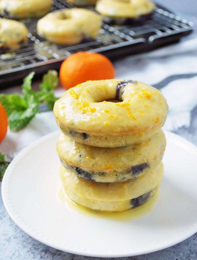 Glazed blueberry donuts stacked on a plate with oranges and fresh mint in the background