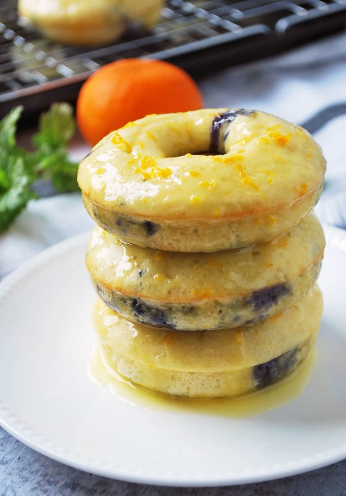 Stack of blueberry protein donuts with orange glaze and donuts in the background