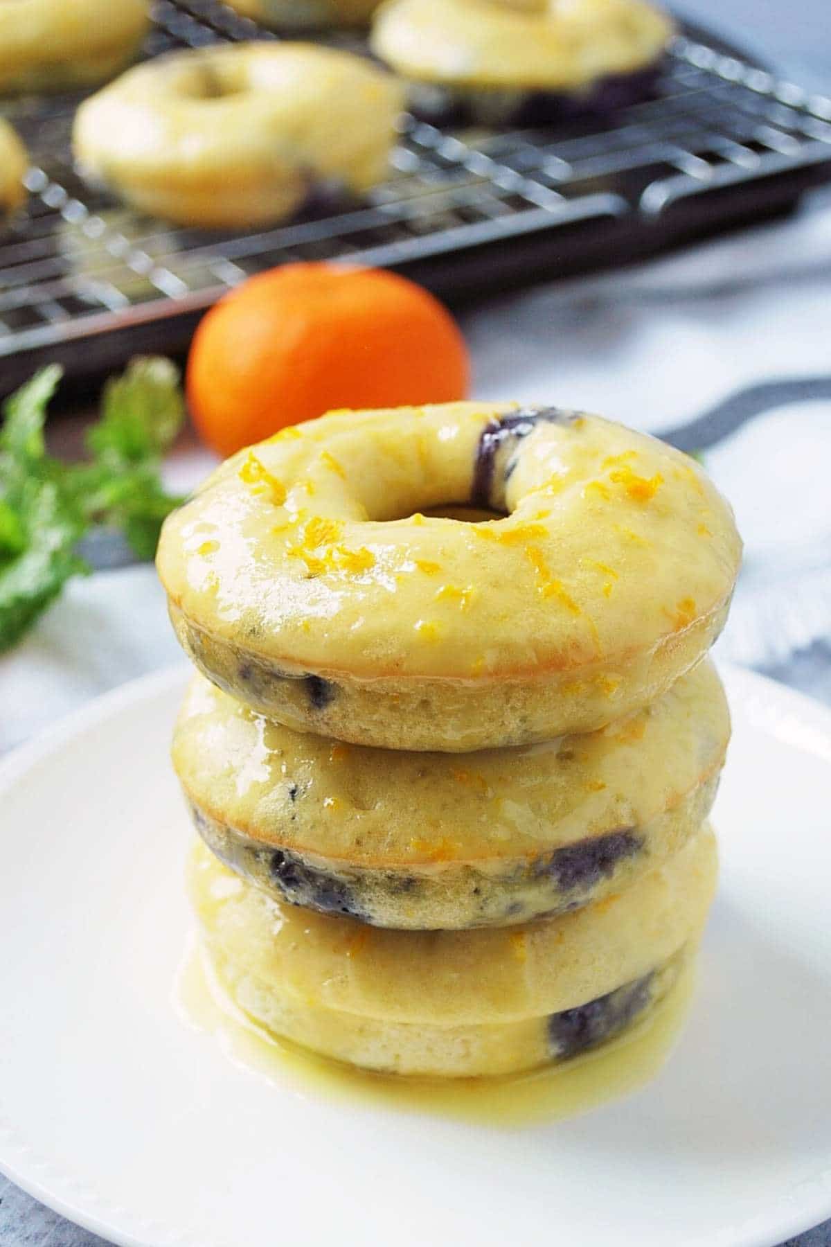 close up of a stack of three blueberry donuts dripping with fresh orange glaze