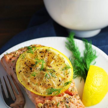 Grilled salmon filet topped with a lemon slice and herbs on a plate