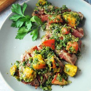 plate of sliced strip steak with peach chimichurri on top