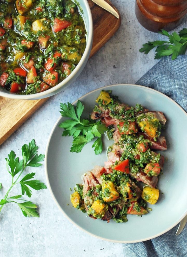 bowl of chimichurri with plate of grilled steak topped with peach chimichurri sauce