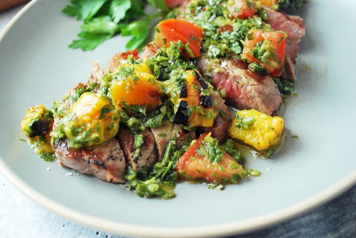 plate of slice grilled New York Strip topped with peach chimichurri sauce