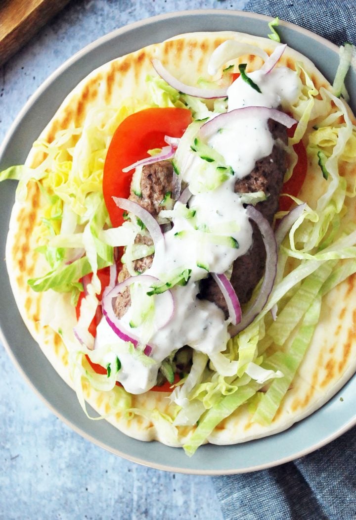 close up photo of kofta wrap with lettuce, tomato, onions and yogurt sauce.