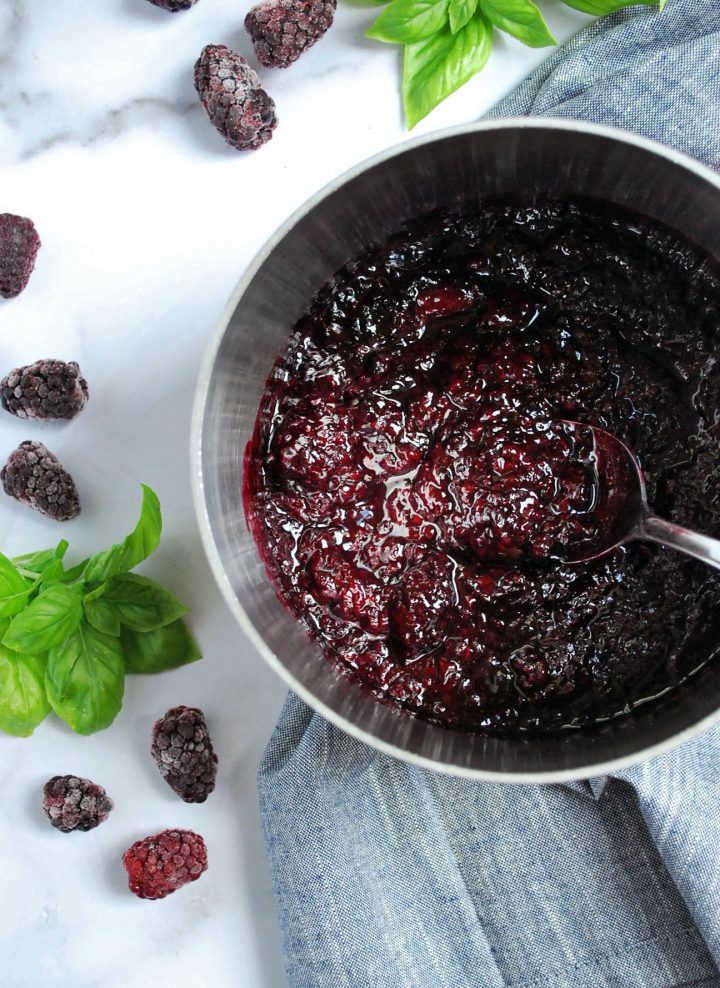 pot of compote with spoon and frozen berries and basil in the background