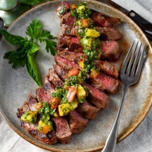a sliced grilled steak with peach and tomato chimichurri sauce and fresh herbs