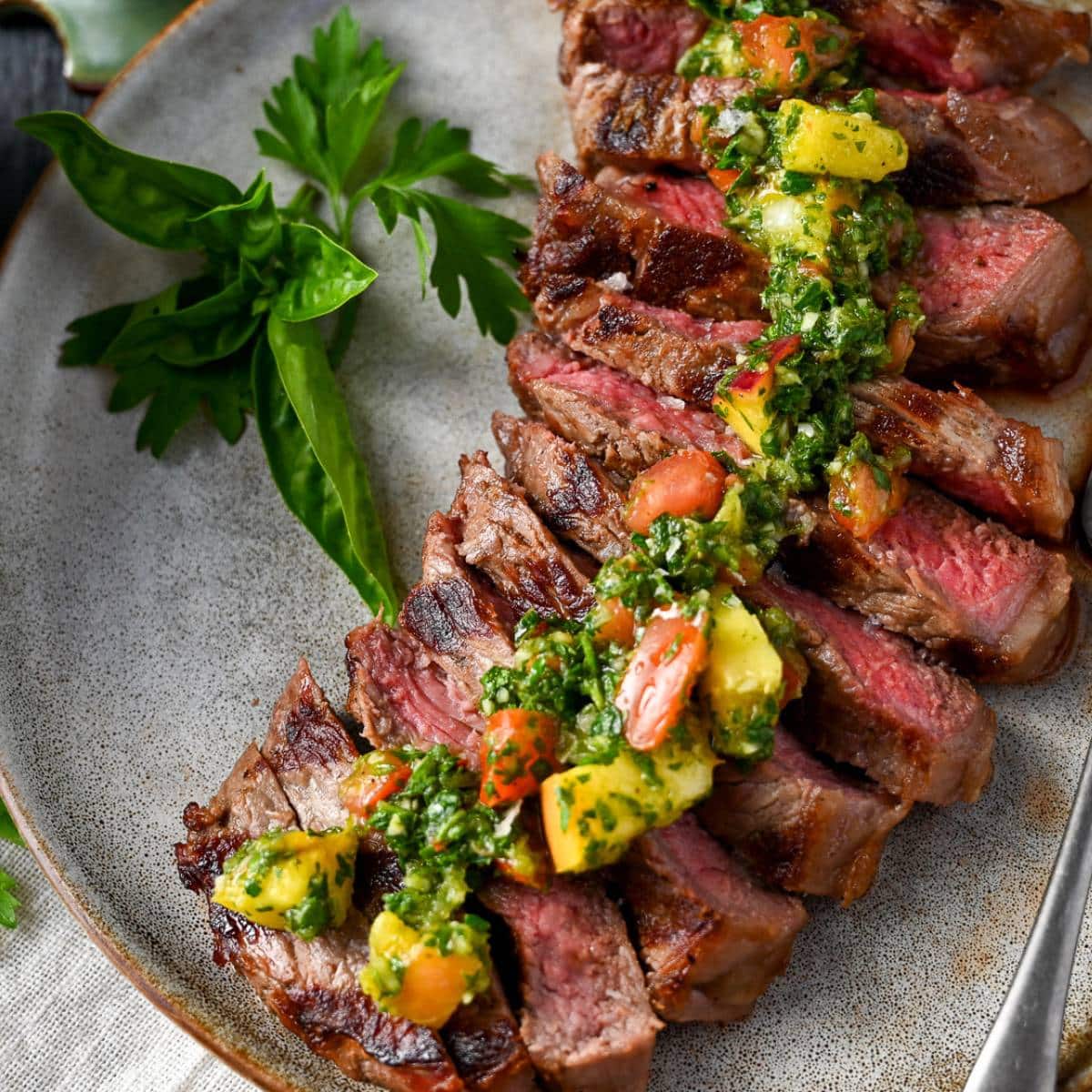 close up of grilled medium rare steak topped with a summer chimichurri sauce