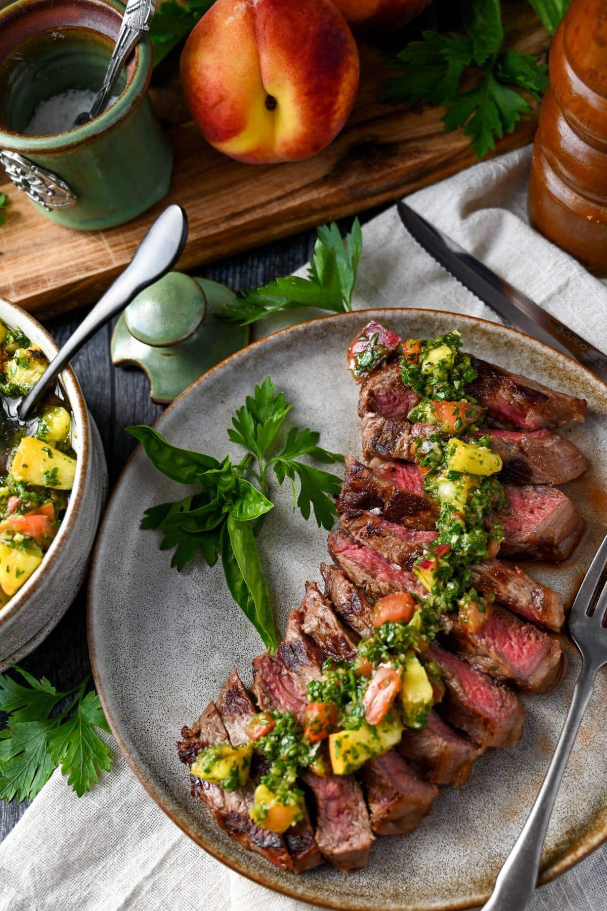 a grilled strip steak with a peach and bowl of salt behind it topped with peach chimichurri
