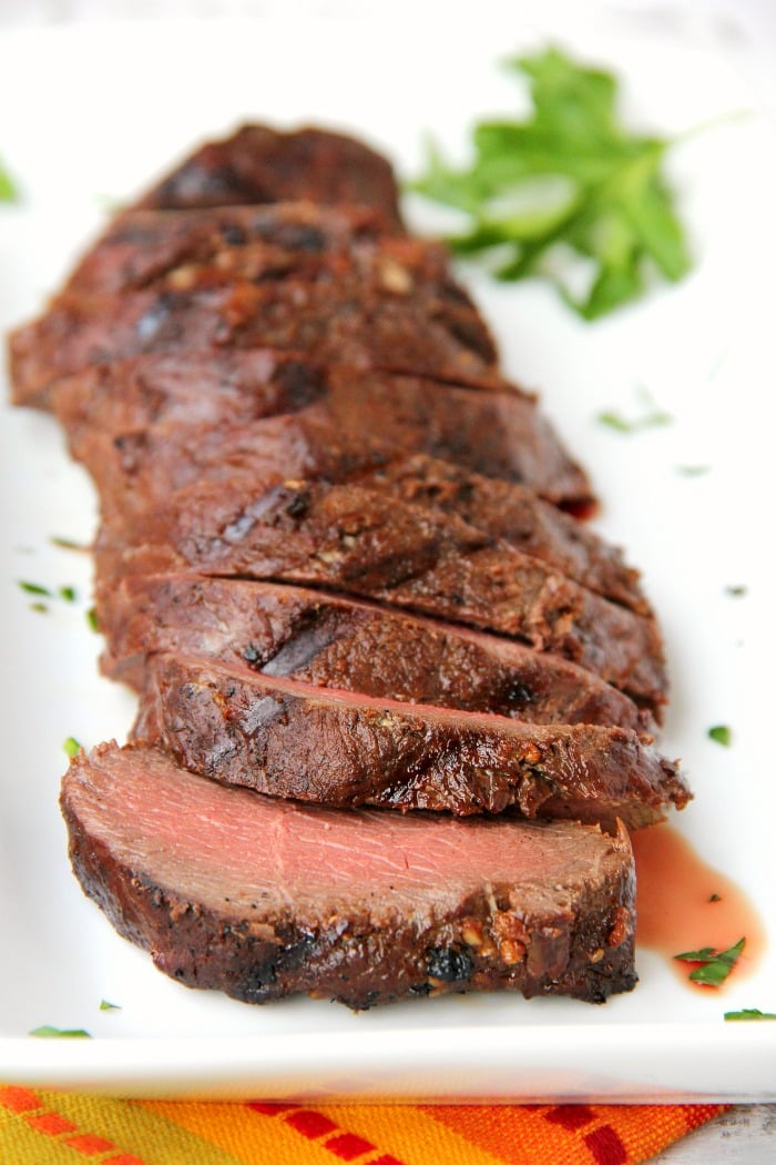 grilled venison backstrap sliced on a platter with fresh herbs