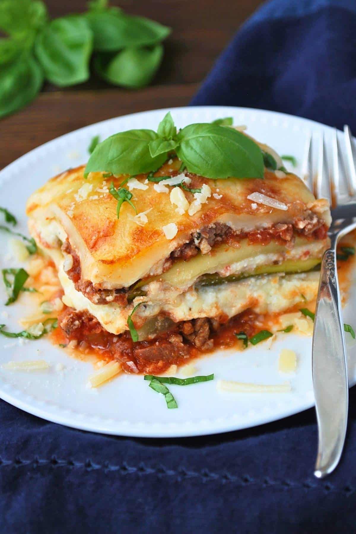 a slice of zucchini lasagna on a plate with fresh basil on top