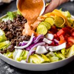 ground venison salad with pickles, tomatoes, and onions with dressing poured on top